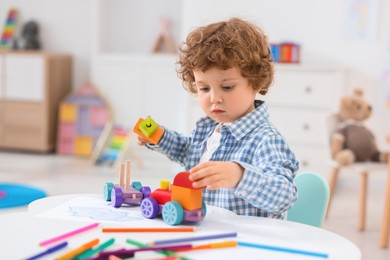 Photo of Cute little boy playing with wooden toys at white table in kindergarten