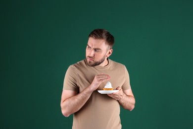 Greedy young man hiding cupcake on green background