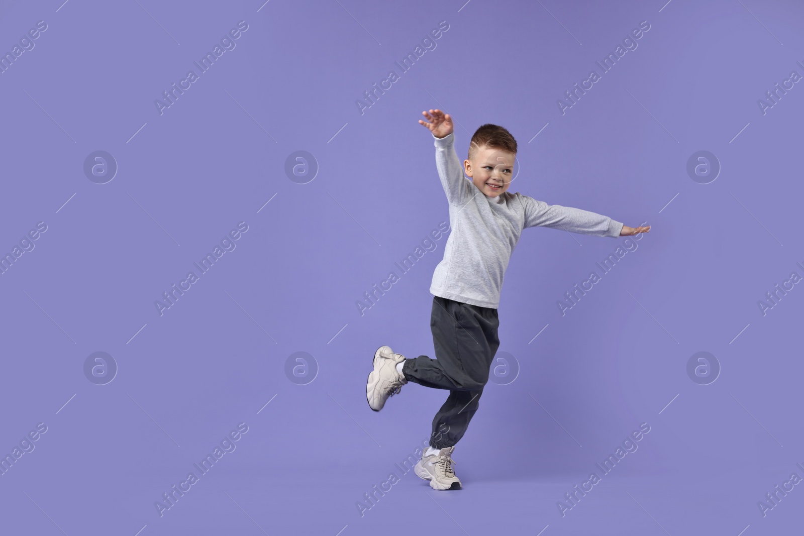 Photo of Happy little boy dancing on violet background. Space for text