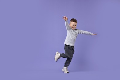 Happy little boy dancing on violet background. Space for text