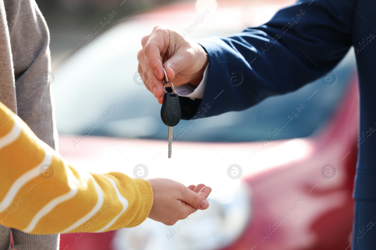 Photo of Salesman giving key to customers in modern auto dealership, closeup. Buying new car