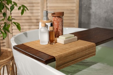 Wooden tray with spa products on bath tub in bathroom