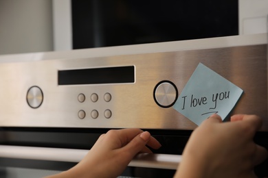 Photo of Woman with sticky note saying I Love You near oven in kitchen, closeup. Romantic message
