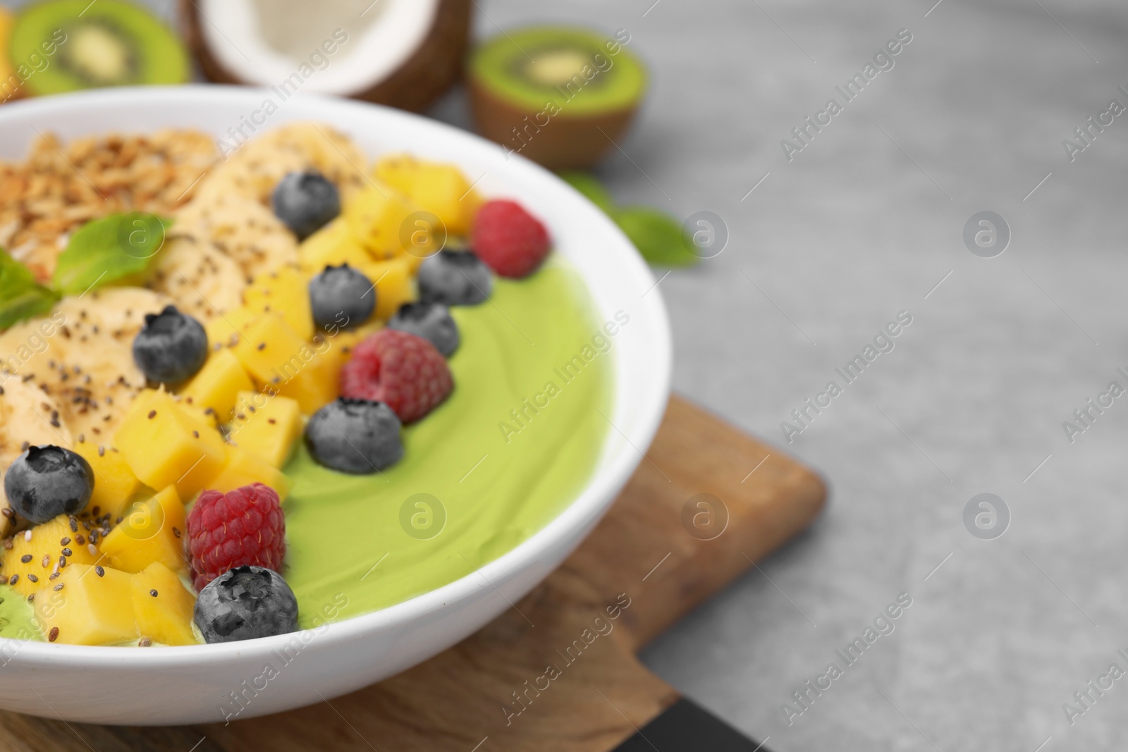 Photo of Tasty matcha smoothie bowl served with fresh fruits and oatmeal on grey table, closeup with space for text. Healthy breakfast