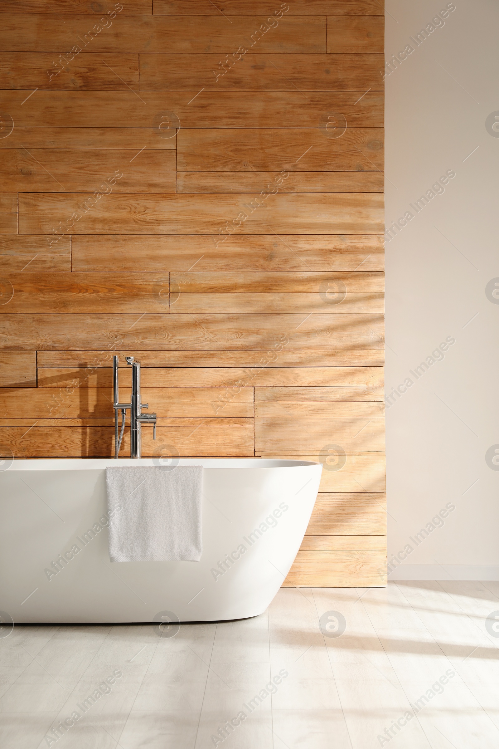 Photo of White bathtub with towel near wooden wall in room