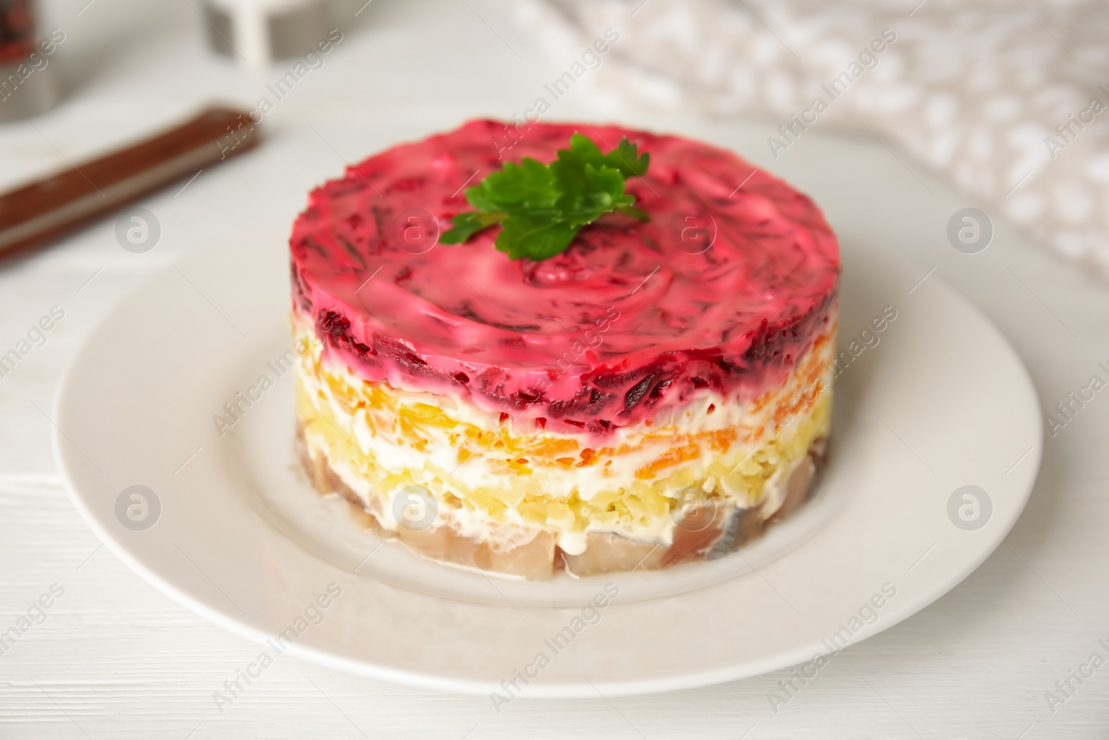 Photo of Herring under fur coat served on white table, closeup. Traditional russian salad