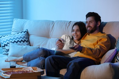 Photo of Happy couple watching TV with pizza on sofa indoors