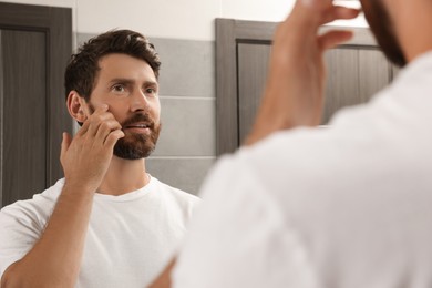 Photo of Handsome man applying cream on face in bathroom