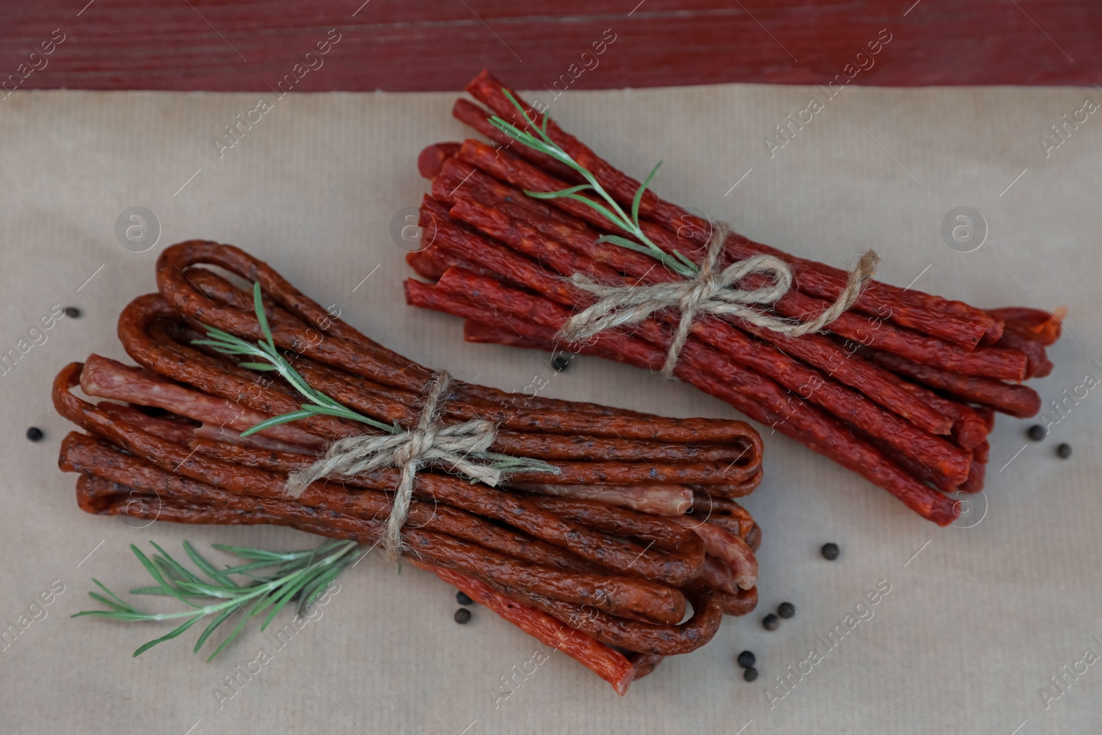 Photo of Tasty dry cured sausages (kabanosy) and spices on parchment paper, flat lay