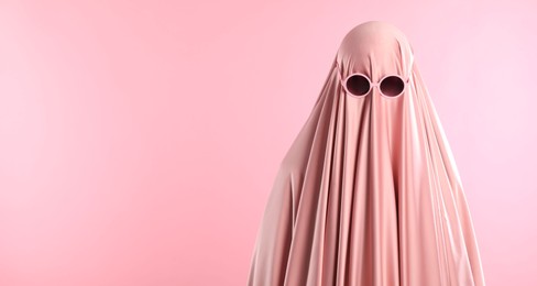 Glamorous ghost. Woman in sheet with sunglasses on pink background, space for text