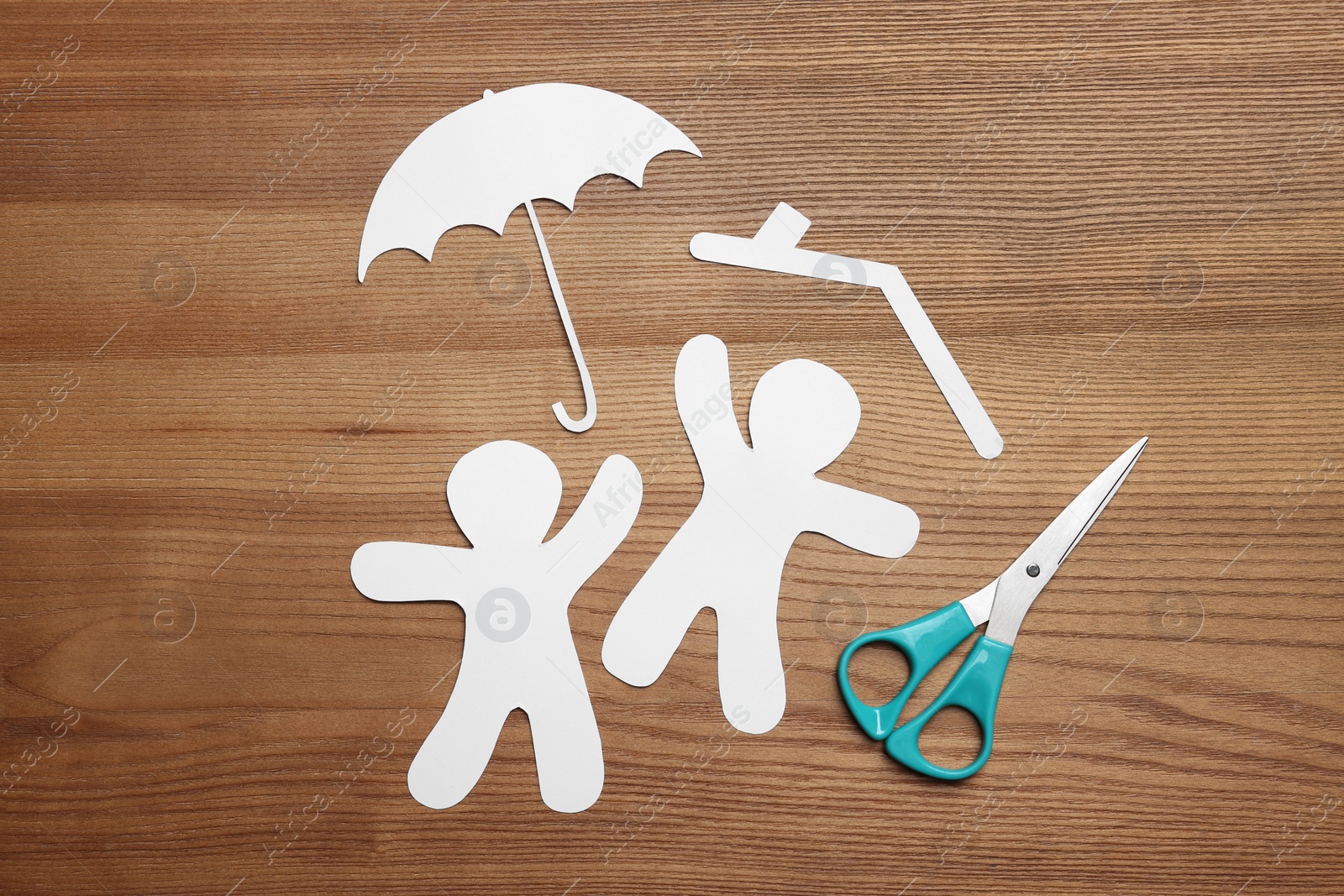 Photo of Flat lay composition with paper silhouettes of people with umbrella and scissors on wooden background. Life insurance concept
