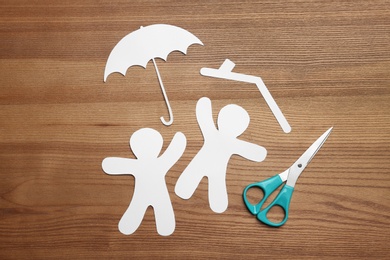 Flat lay composition with paper silhouettes of people with umbrella and scissors on wooden background. Life insurance concept