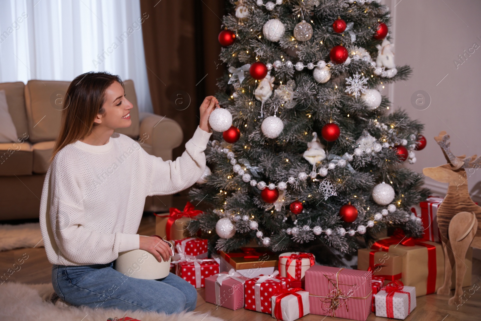 Photo of Young woman decorating Christmas tree at home