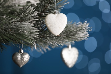 Photo of Beautiful holiday heart shaped baubles hanging on Christmas tree against blue background with blurred festive lights