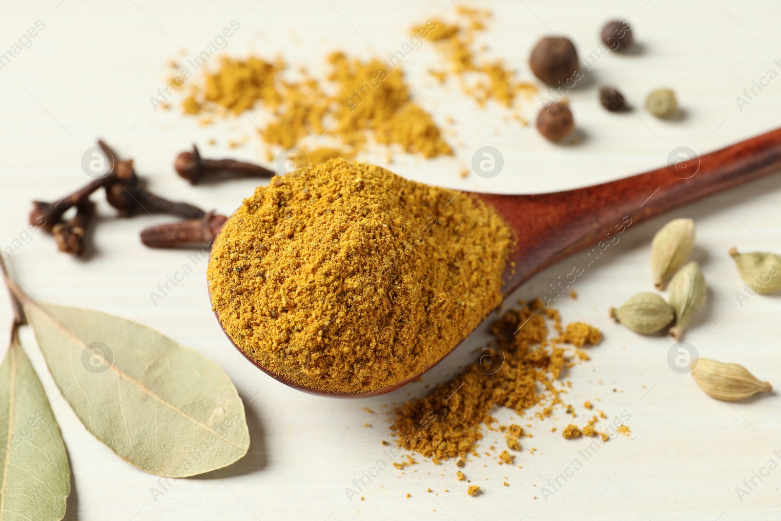 Photo of Spoon with dry curry powder and other spices on light wooden table, closeup