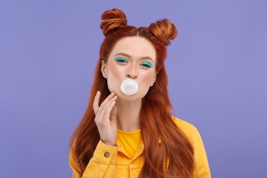 Portrait of beautiful woman with bright makeup blowing bubble gum on violet background