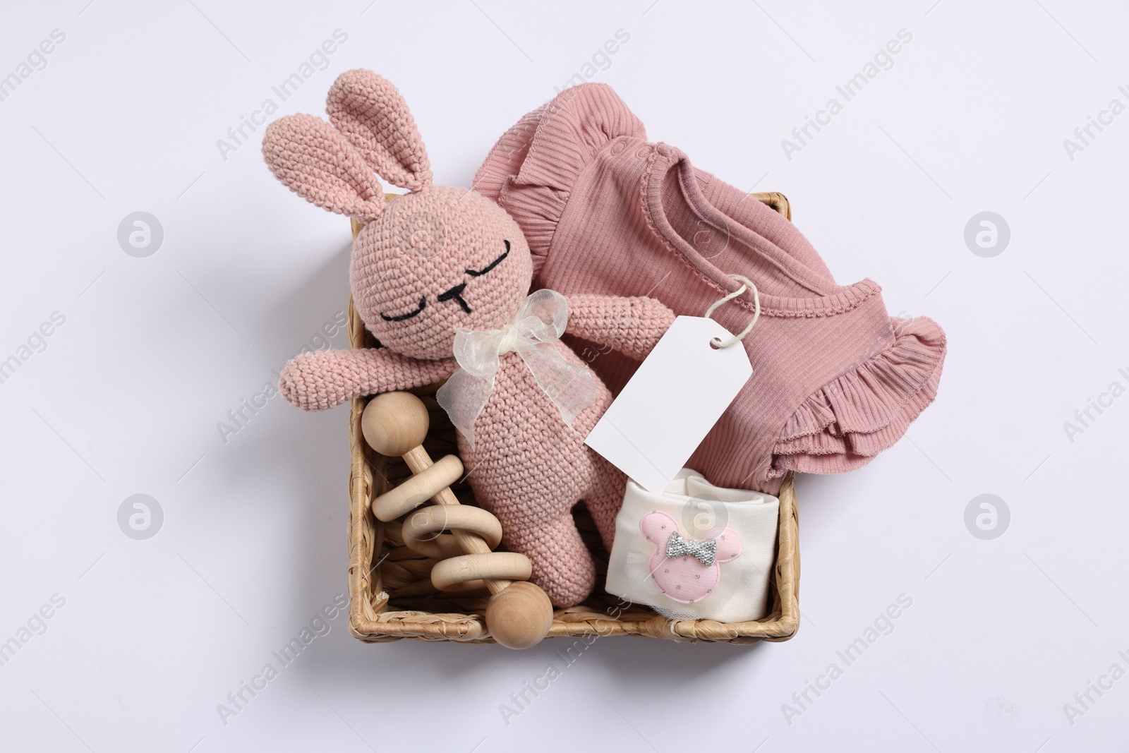 Photo of Different baby accessories, clothes and blank card in wicker box on white background, top view