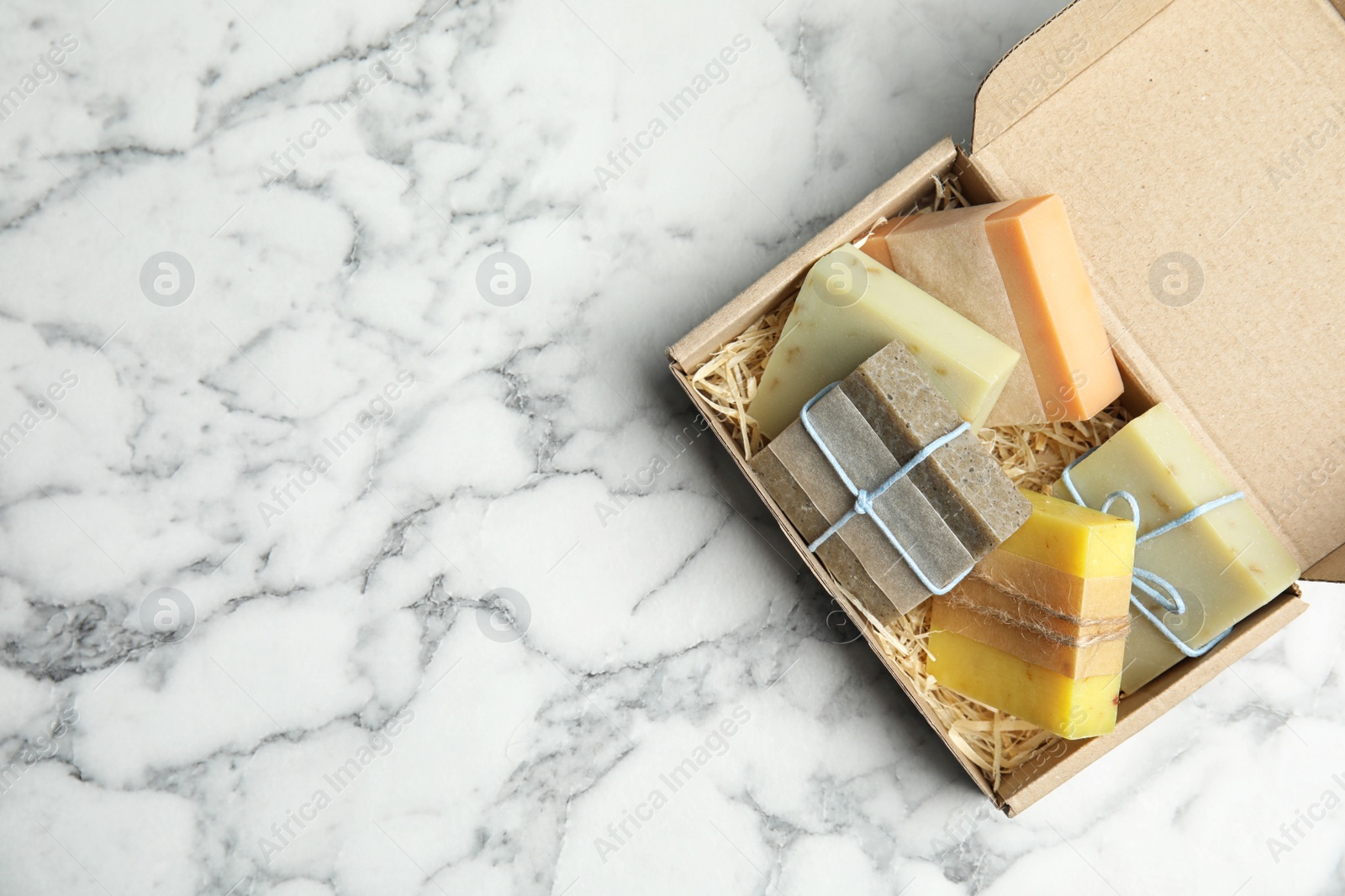 Photo of Cardboard box with different handmade soap bars and space for text on table, top view