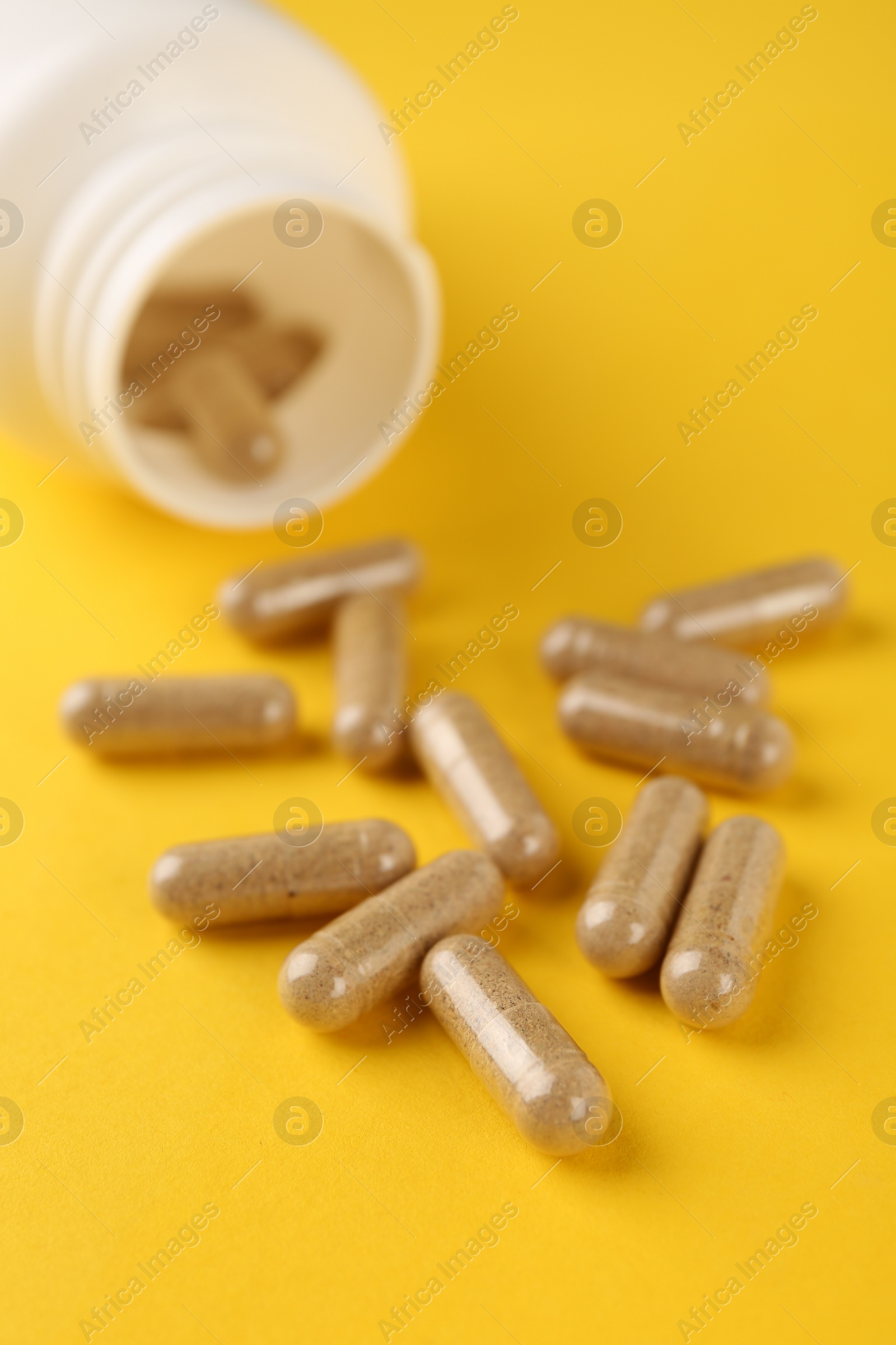 Photo of Vitamin capsules and medical bottle on yellow background, closeup