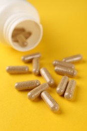 Photo of Vitamin capsules and medical bottle on yellow background, closeup