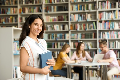 Photo of Happy young woman with books in library. Space for text