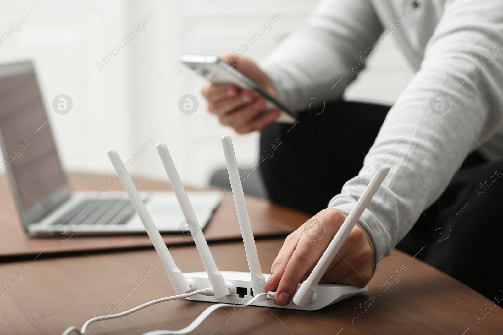 Photo of Man with smartphone and laptop connecting to internet via Wi-Fi router at wooden table, closeup