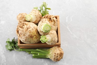 Fresh raw celery roots and wooden crate on light grey table, above view. Space for text