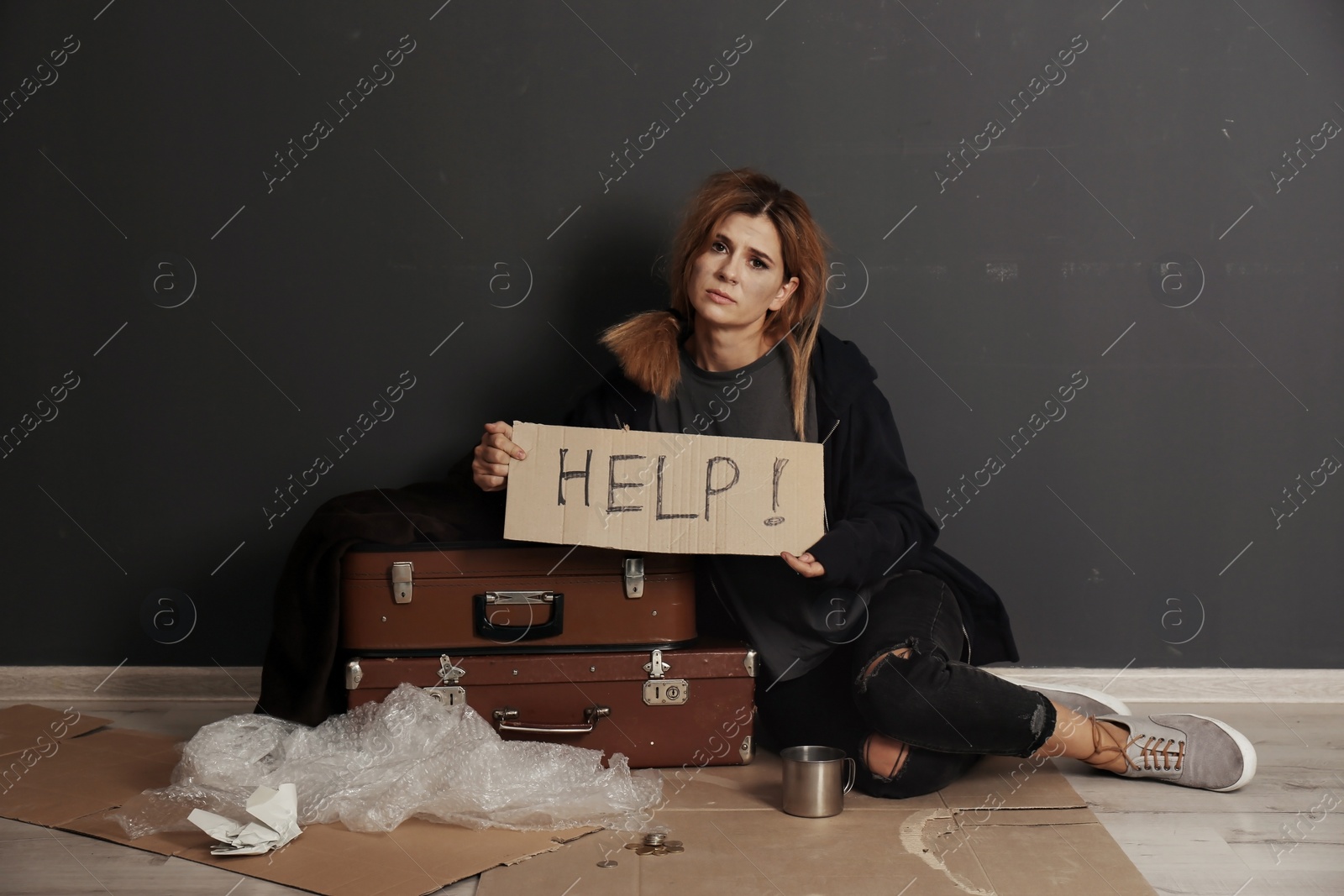 Photo of Poor homeless woman asking for help on floor near dark wall