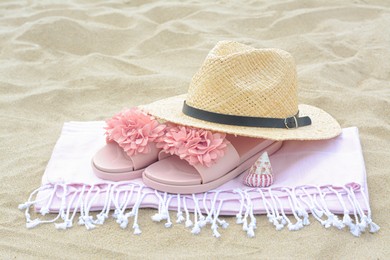 Photo of Blanket with slippers, straw hat and seashell on sand outdoors. Beach accessories
