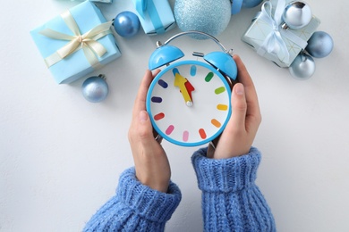 Woman holding alarm clock near Christmas decor over white background, top view. New Year countdown