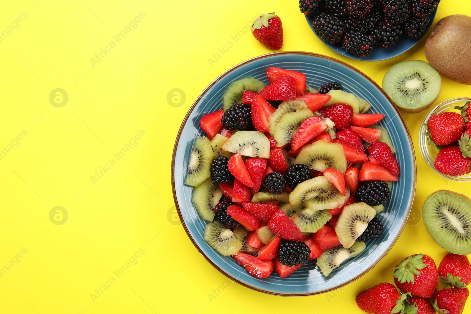 Photo of Plate of yummy fruit salad and ingredients on yellow background, flat lay. Space for text