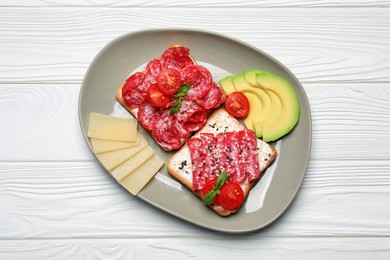 Photo of Tasty toasts with slices of sausages, tomatoes and cheese on white wooden table, flat lay