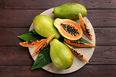 Photo of Fresh ripe papaya fruits with green leaves on wooden table, flat lay