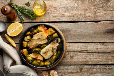 Photo of Pieces of delicious baked cod with vegetables, lemon and spices in dish on wooden table, flat lay. Space for text