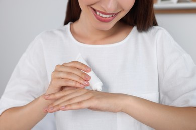 Photo of Happy woman applying cream on her hand indoors, closeup