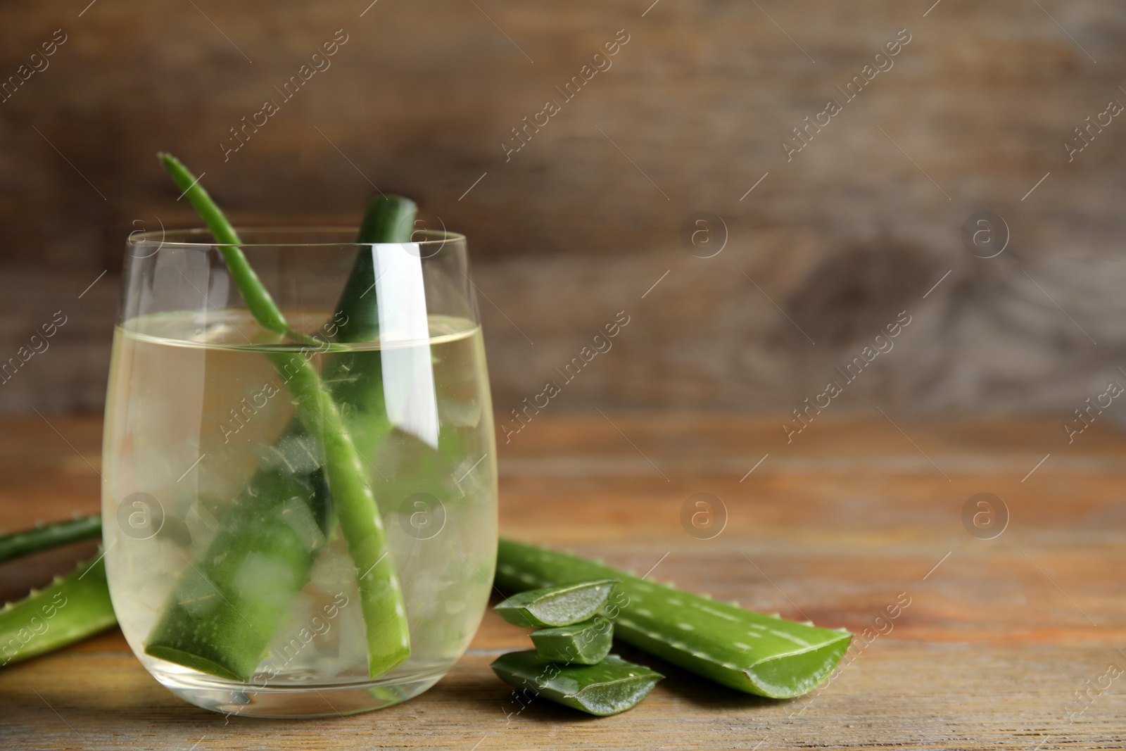 Photo of Fresh aloe drink with leaves in glass on wooden table. Space for text