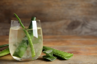 Photo of Fresh aloe drink with leaves in glass on wooden table. Space for text