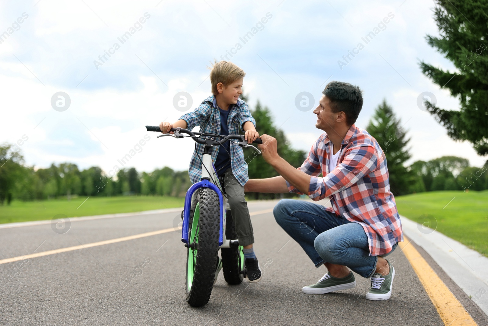 Image of Dad teaching son to ride bicycle outdoors