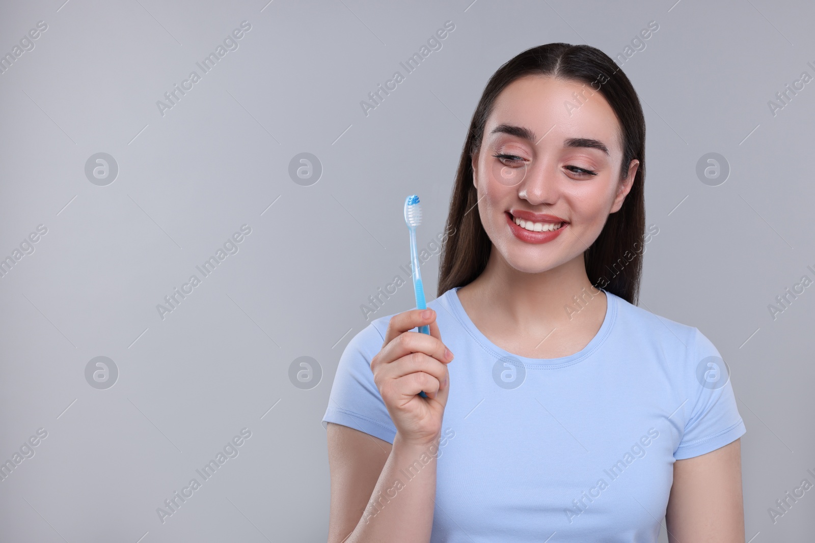 Photo of Happy young woman holding plastic toothbrush on light grey background, space for text