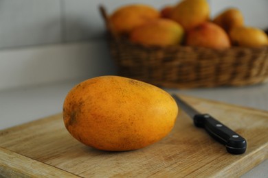 Tasty mango and knife on wooden board indoors