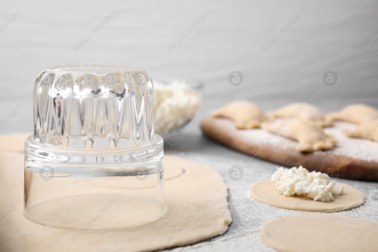 Photo of Process of making dumplings (varenyky) with cottage cheese. Raw dough and ingredients on grey table, closeup