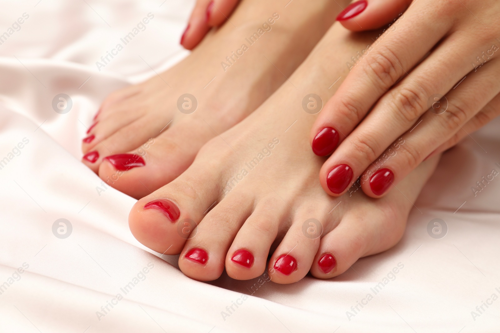 Photo of Woman showing stylish toenails after pedicure procedure and manicured hands with red polish on light silk fabric, closeup