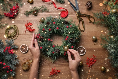 Florist making beautiful Christmas wreath at wooden table, top view