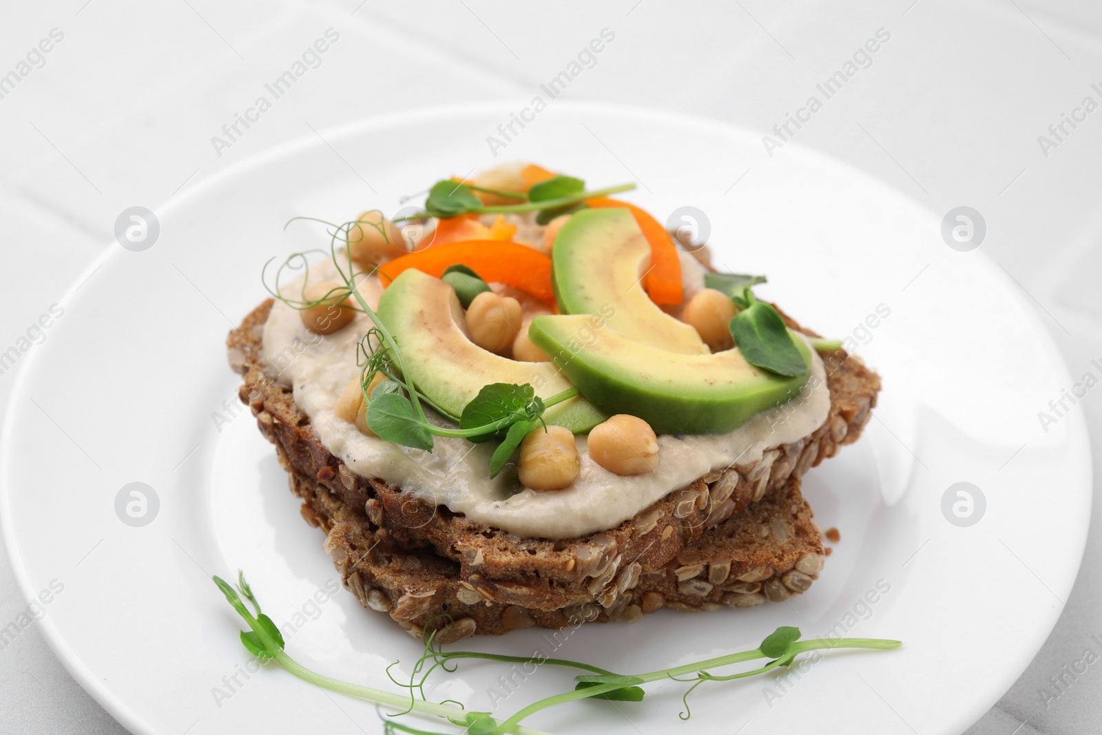 Photo of Tasty vegan sandwich with avocado, chickpeas and bell pepper on white table, closeup