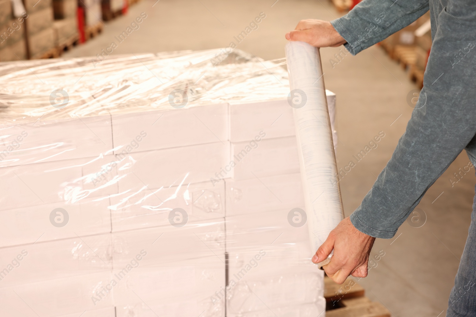 Photo of Worker wrapping boxes in stretch film at warehouse, closeup