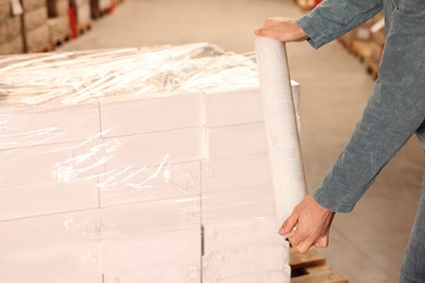 Photo of Worker wrapping boxes in stretch film at warehouse, closeup