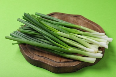 Photo of Wooden board with bunch of fresh spring onion on green background