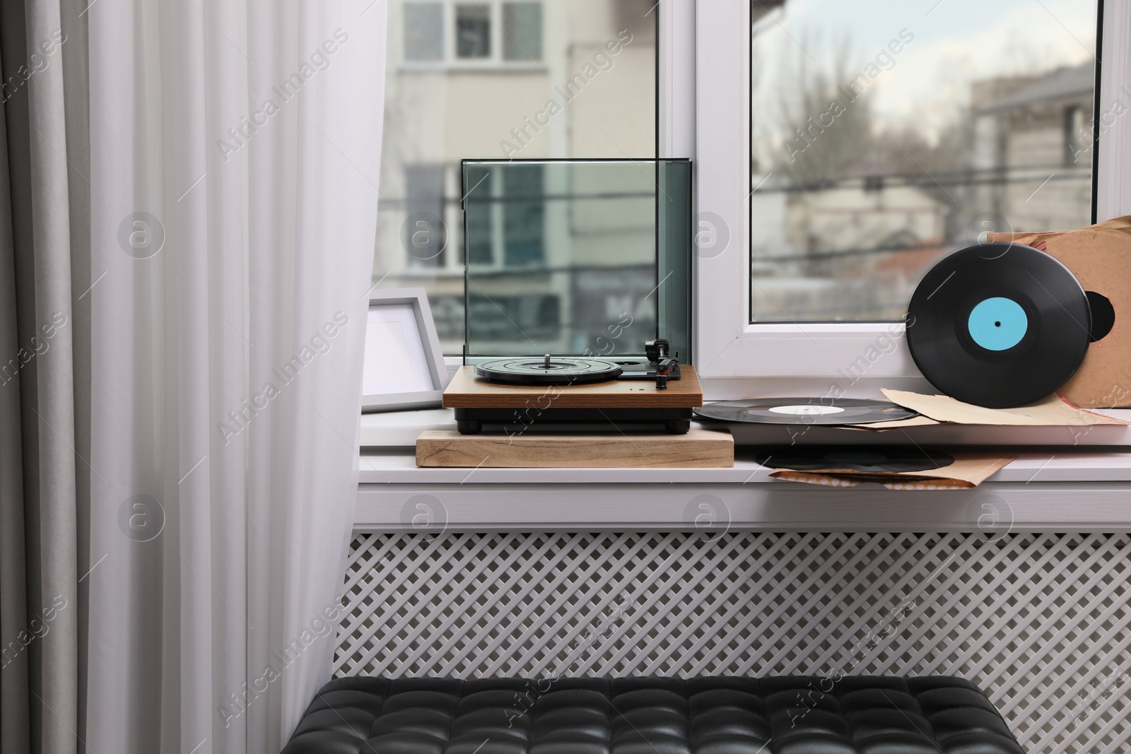 Photo of Stylish turntable with vinyl discs on windowsill in room