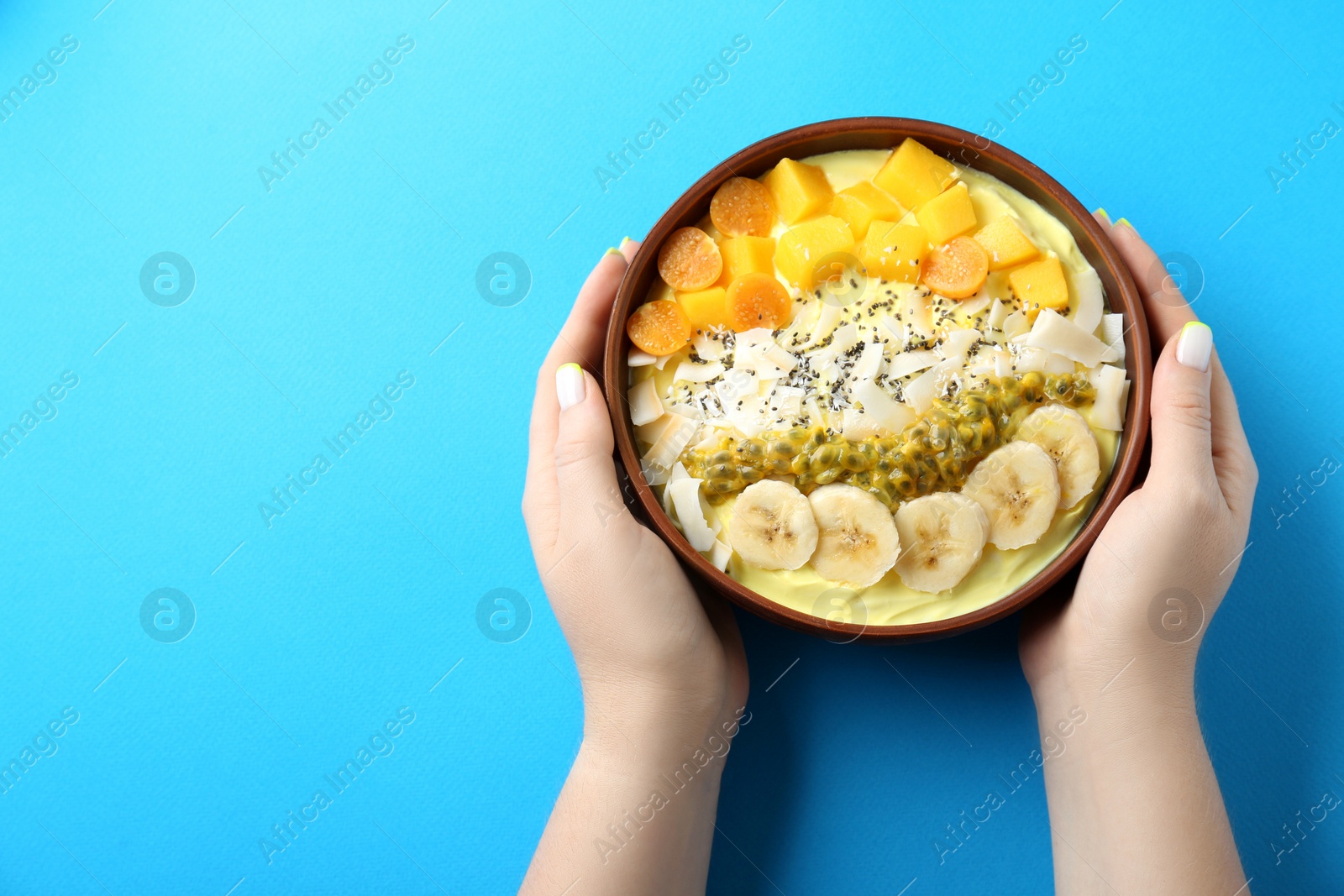 Photo of Woman holding tasty smoothie bowl with fresh fruits at light blue table, top view. Space for text