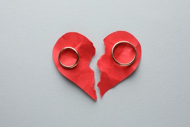 Halves of torn red paper heart and wedding rings on white background, top view. Broken heart